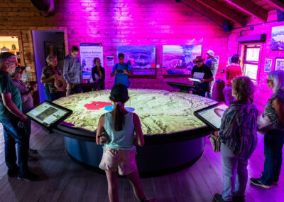 People stand around large round table with map view and interactive pads attached.